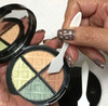 A hand holding a white cosmetic spatula over an eye shadow compact