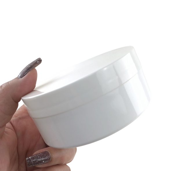 A hand holding a white wide mouth plastic cosmetic jar.