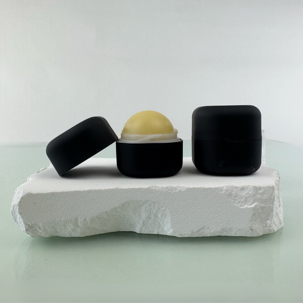 Black lip balm ball with lid on it's side and a closed square lip balm container